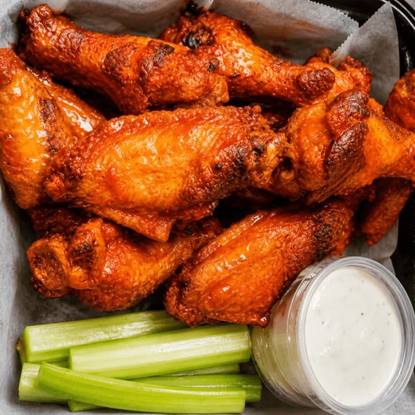 Close-up of a container of buffalo chicken wings with celery sticks and a side of ranch dressing.